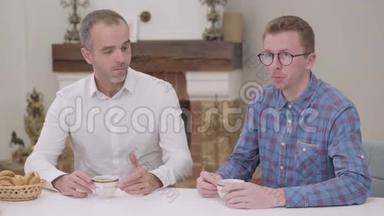 一个戴眼镜的白人男孩和坐在桌子旁的老人说话。 公公做出讽刺的表情